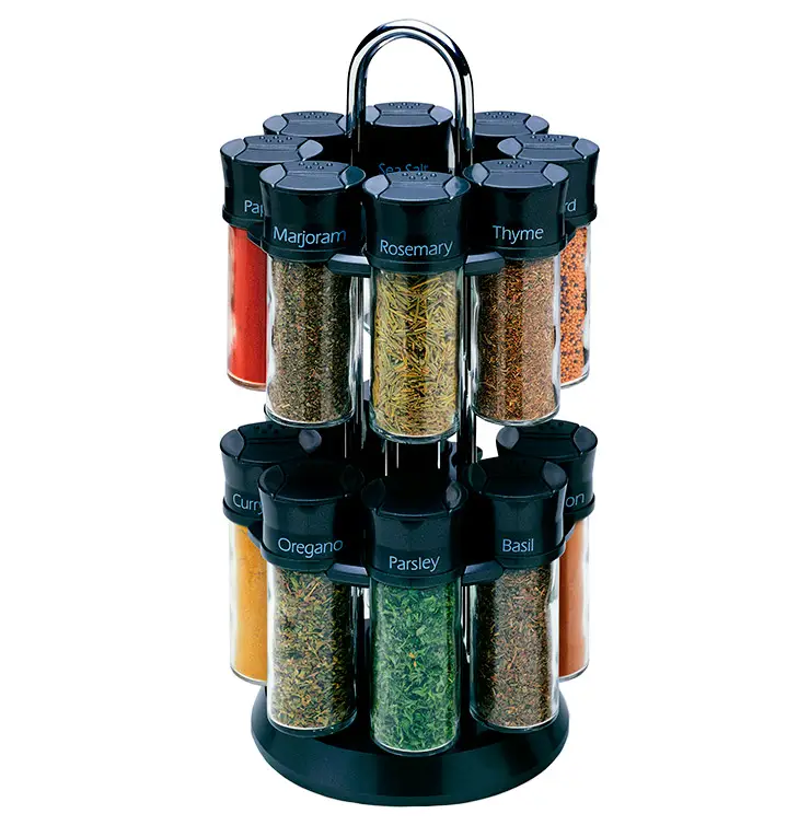 A rotating spice rack with two tiers holding various clear jars filled with different spices. Each jar has a black lid labeled with a spice name, such as rosemary, thyme, oregano, and basil. The rack is stainless steel and black.