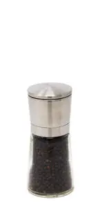 A transparent pepper grinder with a stainless steel top is filled with whole black peppercorns. The clear body reveals the dark pepper inside, standing against a plain white background.