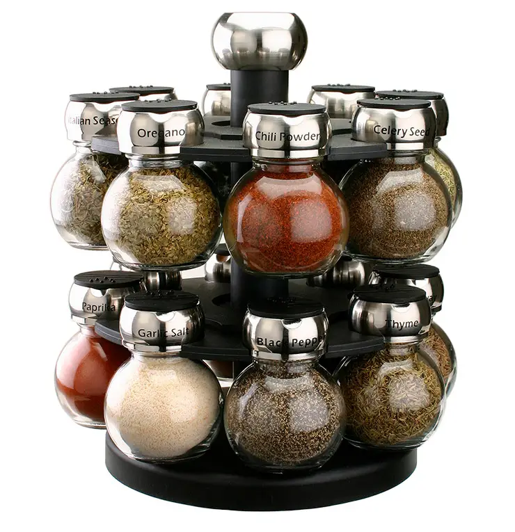 A rotating spice rack with twelve spherical glass jars, each labeled and filled with different spices like chili powder, oregano, celery seed, paprika, and black pepper. The rack has a modern, metallic design.