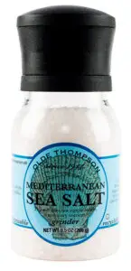 A clear plastic grinder bottle with a black top, labeled Olde Thompson Mediterranean Sea Salt on a light blue label. The bottle contains coarse white sea salt. Net weight is 9.5 oz (269 g).