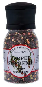 A clear plastic pepper grinder filled with multi-colored peppercorns. The label reads Olde Thompson PEPPER SUPREME Grinder and indicates it contains 136g. The lid is black and the container is recyclable.