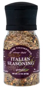 A clear spice grinder filled with a mix of dried herbs labeled Olde Thompson Italian Seasoning. The label mentions since 1941 and net wt. 3.1 oz (87.8g). It is recyclable and disposable.