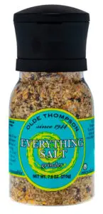 A grinder bottle of Olde Thompson Everything Salt, containing a mix of spices and salt. The label features blue and yellow colors, with text indicating its recyclable and weighs 7.6 oz (215g).