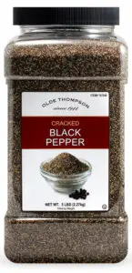 A large plastic container of Olde Thompson cracked black pepper, labeled as 5 pounds (2.27 kg). The label features an image of a bowl of cracked black pepper with a few scattered peppercorns.