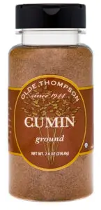 A clear plastic spice jar with a black lid labeled Olde Thompson since 1944 Cumin ground. The label is brown with an illustration of cumin plants. The net weight is 7.6 oz (216.6g).