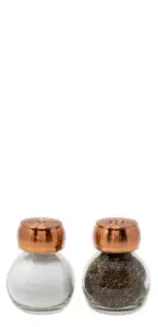 Salt and pepper shakers with copper tops. The salt shaker is on the left, containing white salt, and the pepper shaker is on the right with dark pepper granules. The containers are made of clear glass.