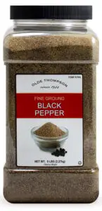 A large plastic container of Olde Thompson fine ground black pepper, labeled with a design featuring a small glass bowl filled with ground pepper and whole peppercorns. The container has a capacity of 5 pounds (2.27 kg).