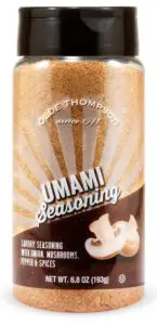 Bottle of Olde Thompson Umami Seasoning, featuring a design of sun rays and an image of onions and mushrooms. The label describes it as a savory seasoning with onion, mushrooms, pepper, and spices. Net weight is 6.8 oz (193g).