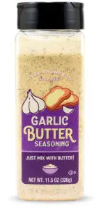 A clear bottle labeled Garlic Butter Seasoning by Olde Thompson, featuring images of garlic and buttered bread. The bottle contains 11.5 oz (326g) and suggests mixing with butter. The label is purple with white and orange accents.