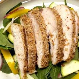Sliced, breaded chicken breast dusted with Cacio e Pepe seasoning, served on a bed of fresh spinach, yellow bell pepper strips, red onion, and zucchini slices.